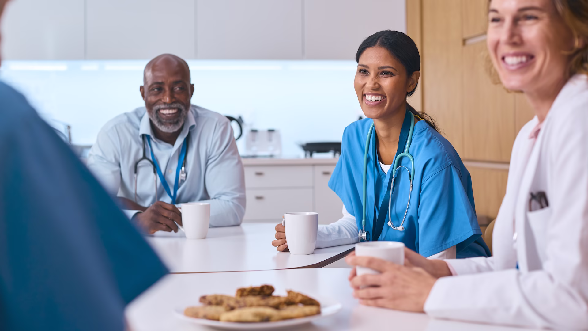 multi-cultural-medical-team-taking-coffee-break-in-2026-01-05-22-59-37-utc Nurses smiling and talking over a meal